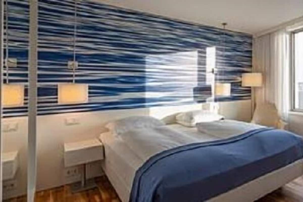 A modern hotel room with a bed, bedside tables, and a view of the outdoors.