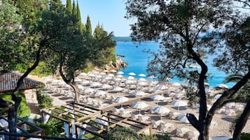 A beach with rows of sun loungers and umbrellas, a wooden deck, and a view of the sea.