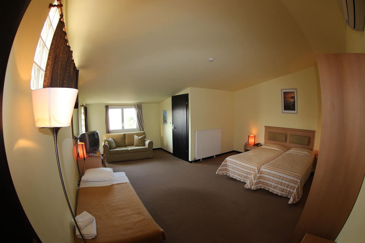 A hotel room with two beds, a sofa, a TV, and a window with curtains.