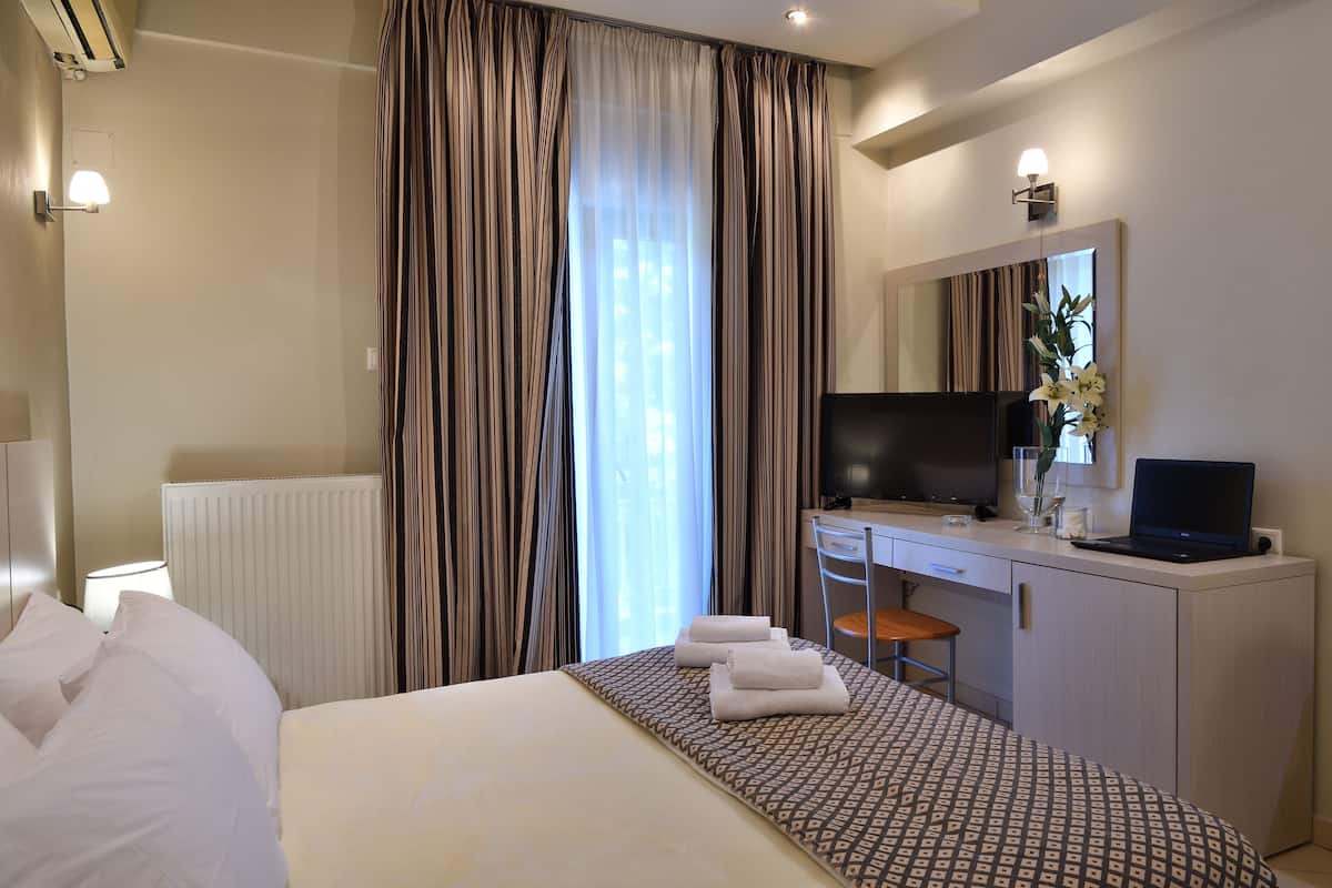 A hotel room with a bed, a desk with a chair, a TV, and a large window with curtains.