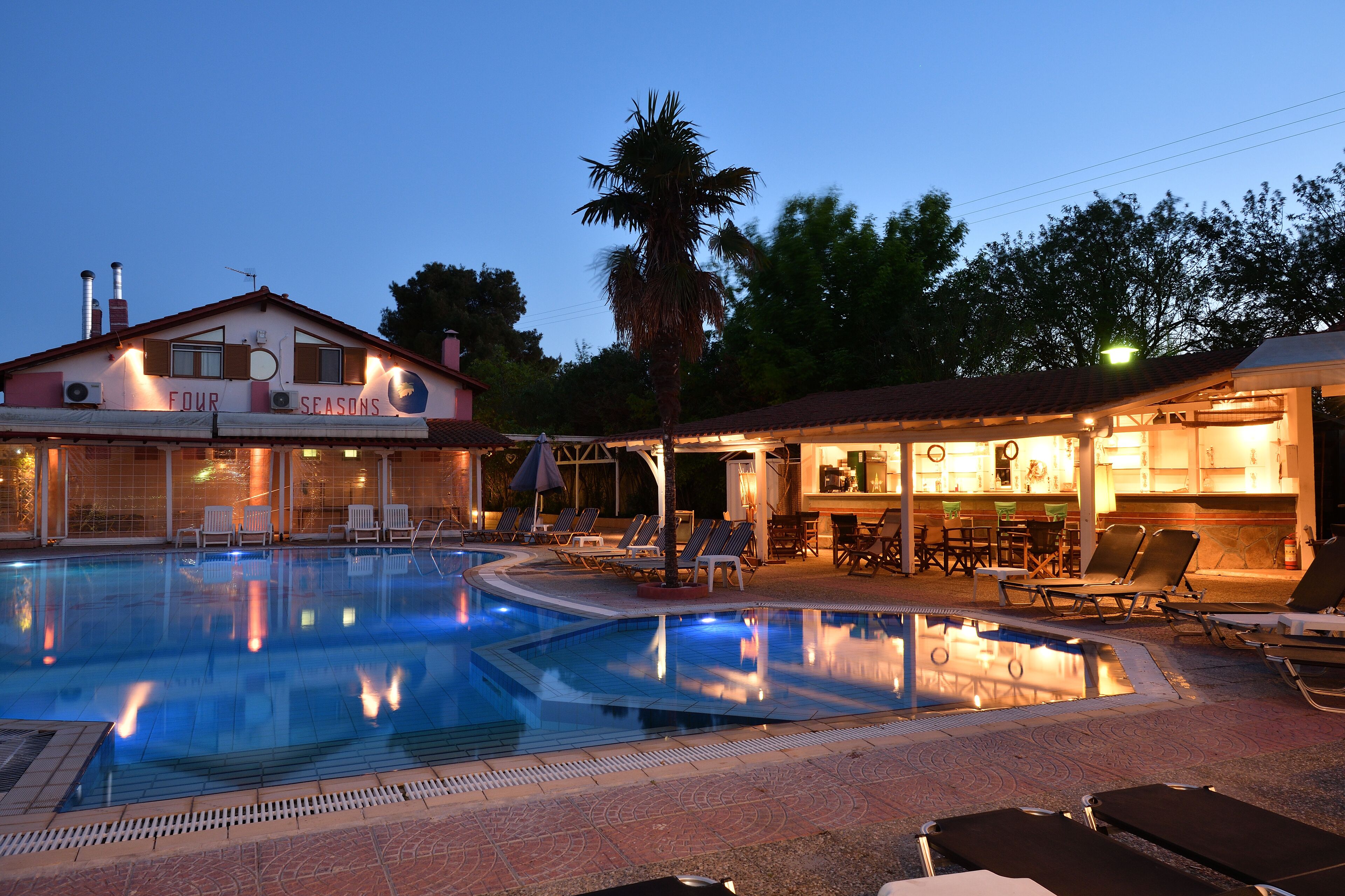 Ein Schwimmbecken mit Liegestühlen, einer Bar und einem Gebäude mit der Aufschrift "FOUR SEASONS".