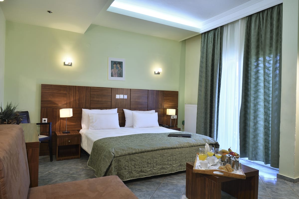 A hotel room with a large bed, bedside tables, a desk with breakfast items, and a window with curtains.