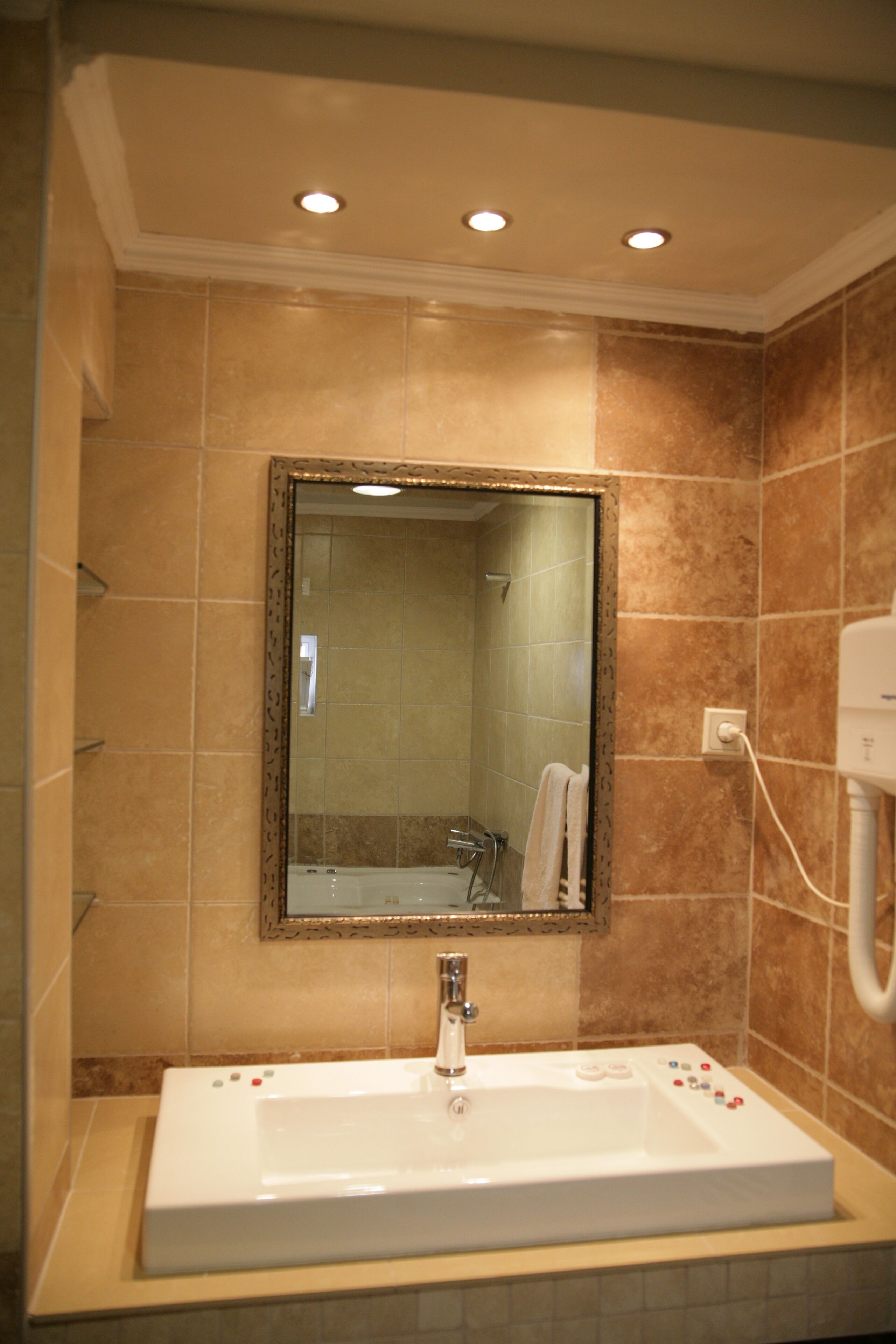 A bathroom with a large mirror, a white sink, and beige tiles.