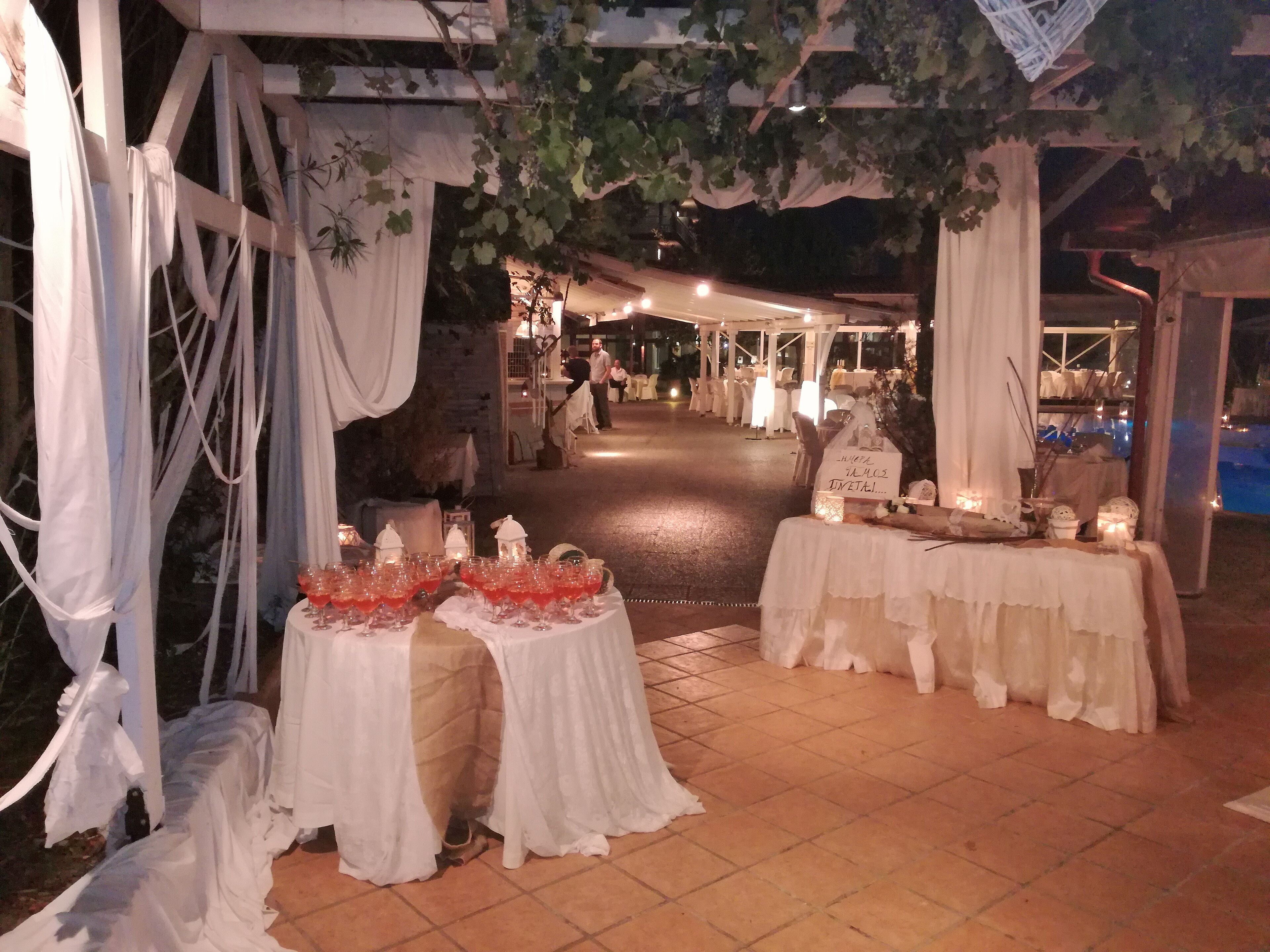 Et udendørs eventområde med borde dækket til en reception, dekoreret med hvide gardiner og stearinlys.