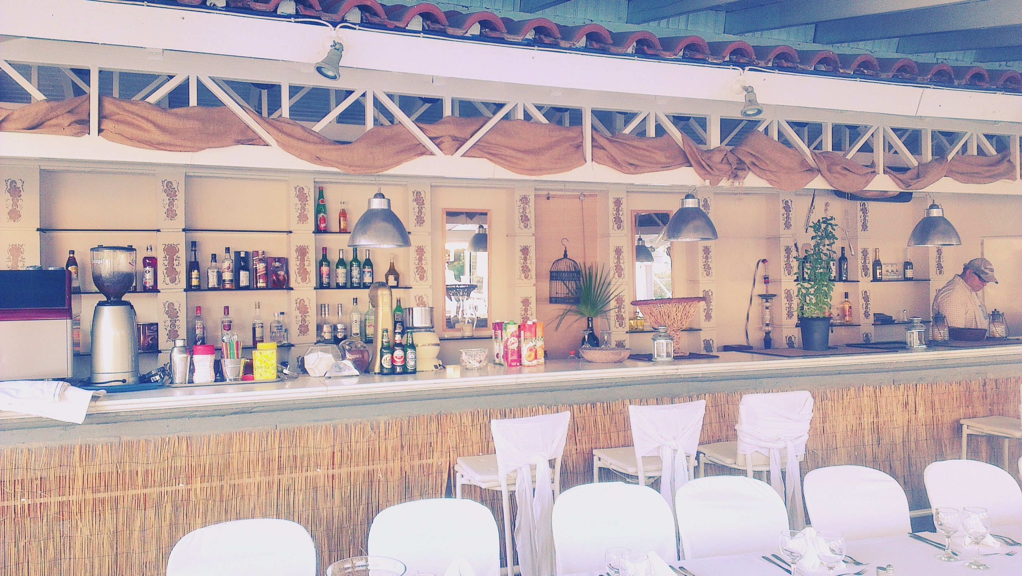 A bar area with a counter, shelves with bottles, and chairs arranged for seating.
