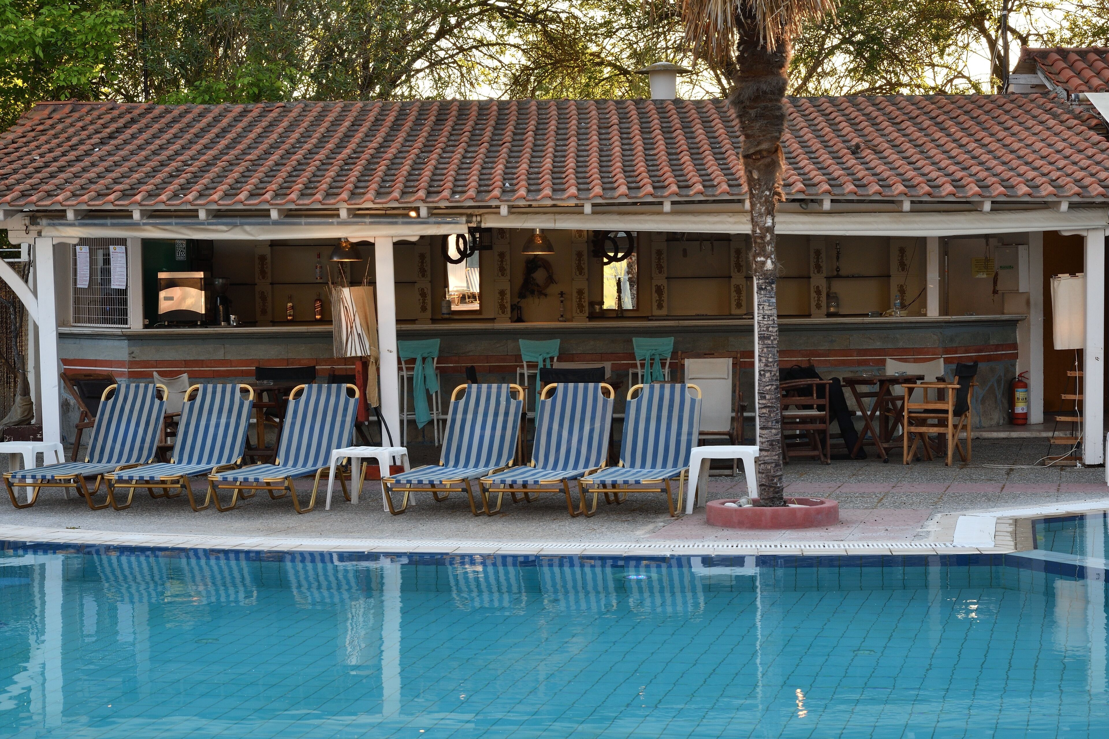 A pool area with lounge chairs, a covered seating area, and a building with a tiled roof.