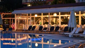 A poolside area with lounge chairs and umbrellas, a covered seating area, and a reflection in the pool. - Four Seasons Hotel (Thermi)