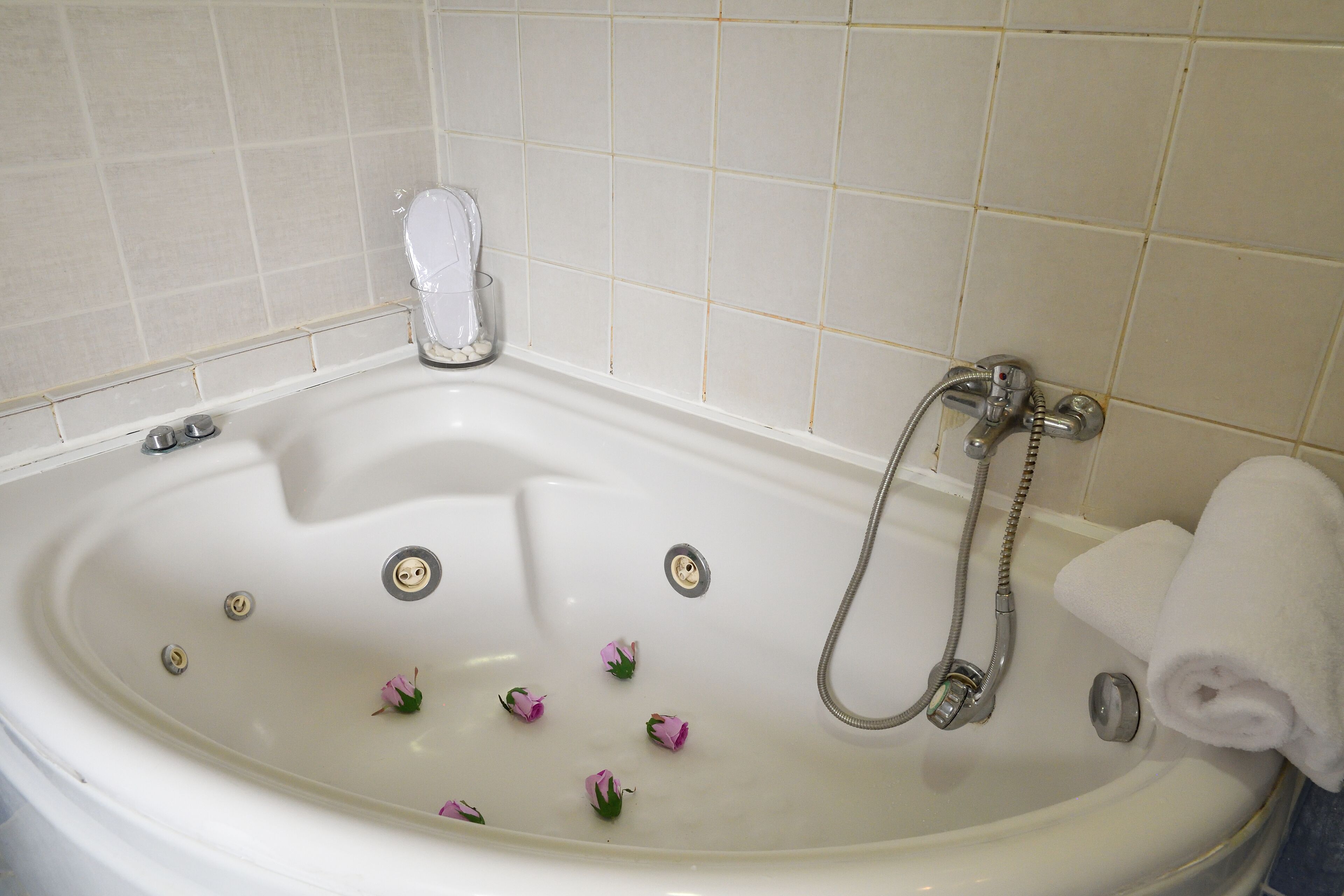 A white bathtub with a shower head, a glass of water, and a rolled towel.