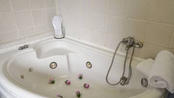 A white bathtub with a shower head, a glass of water, and a rolled towel.