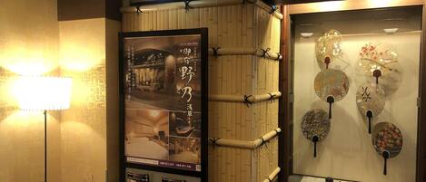 Vestíbulo de hotel con decoración tradicional japonesa, que incluye una pared de bambú y una exhibición de abanicos decorativos.