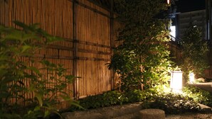 En nattbild av en traditionell japansk trädgård med ett bambustaket, en stenlampa och grusgångar.