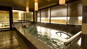 Ett område med ett bubbelbad, kakelgolv, en glasvägg och ett fönster med persienner.