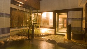 Ett traditionellt japanskt onsen med ett stenbad, bambuväxter och utsikt över omgivningen genom stora glasdörrar.