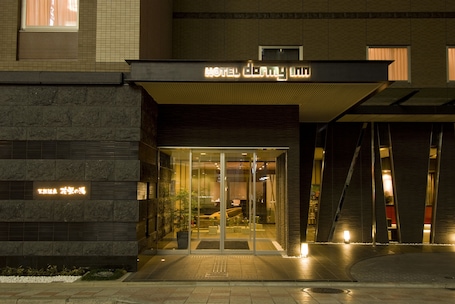 Entrada de hotel con diseño moderno, destacando un acceso de vidrio y un cartel sobre la puerta.