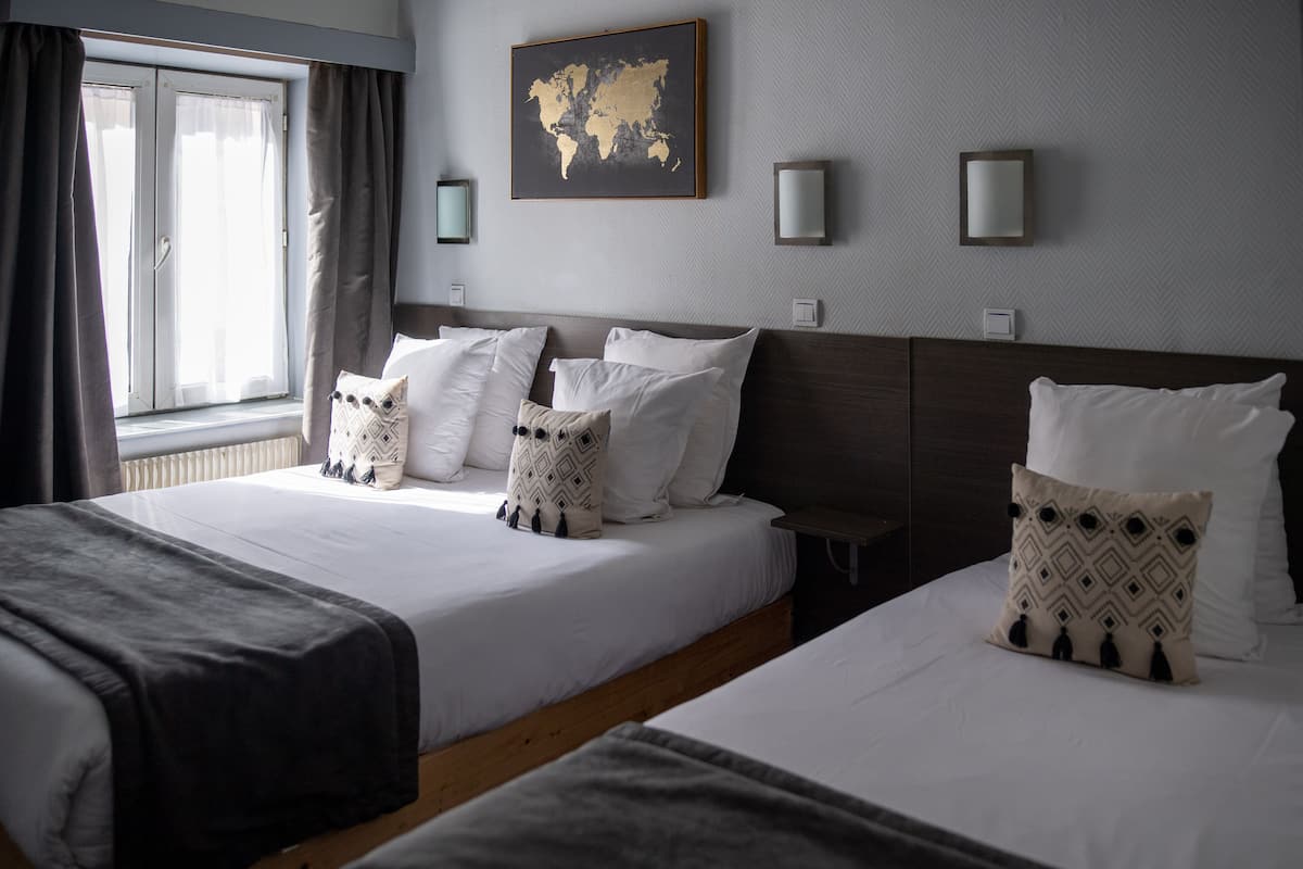 Habitación de hotel con dos camas, un mapa mundial en la pared y una ventana con cortinas.