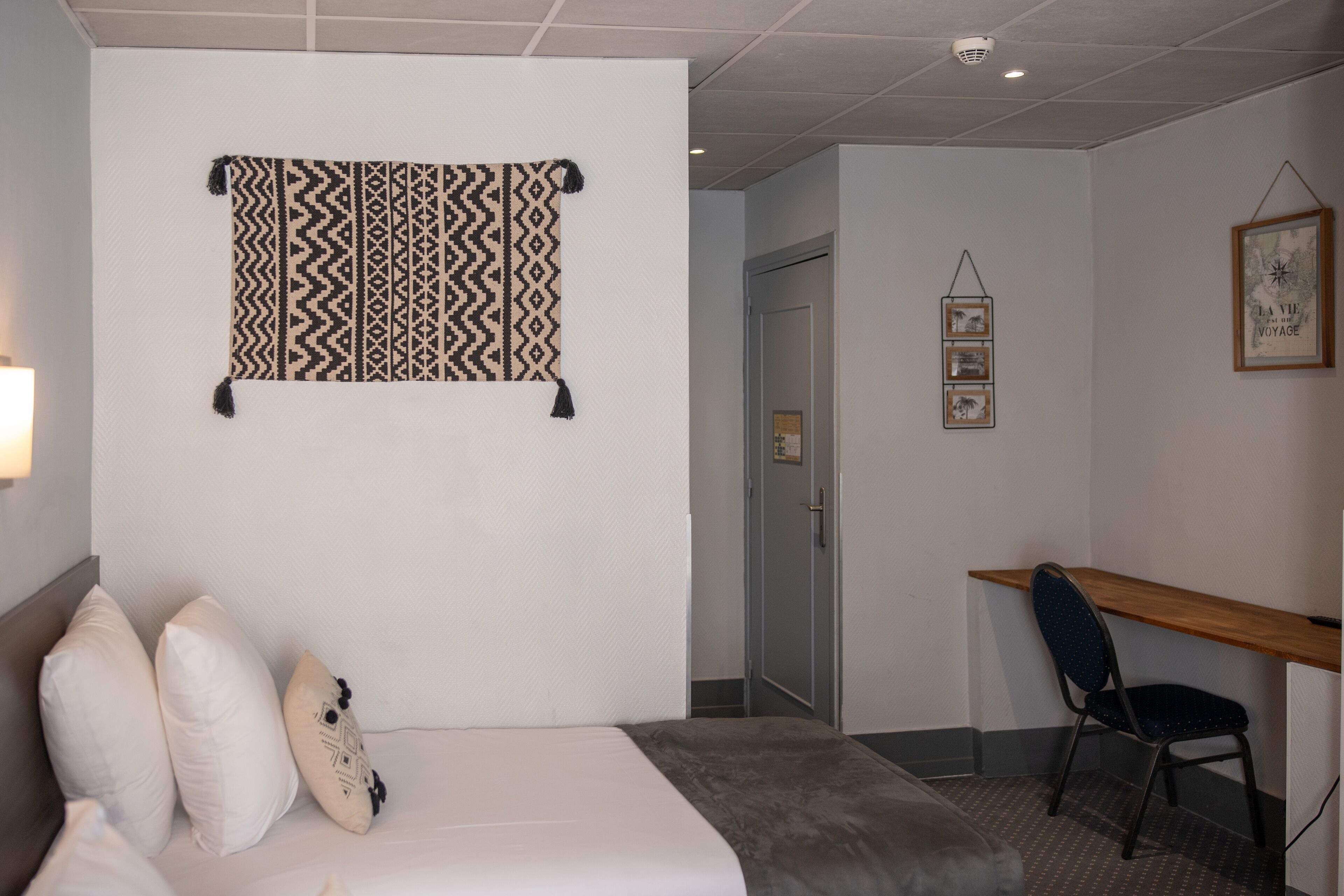 A hotel room with a bed, pillows, a desk, and a wall-mounted tapestry.