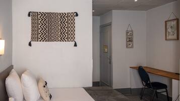 Habitación de hotel con una cama, almohadas, un escritorio y un tapiz colgado en la pared.