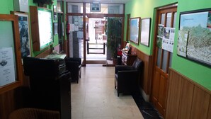 A reception area with a reception desk, black leather chairs, framed pictures on the walls, and a green wall. - Pension Monteverde (Cangas de Onis)