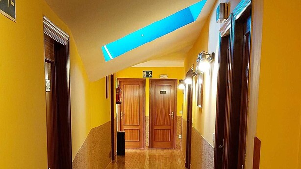 A hotel hallway with wooden flooring, yellow walls, and multiple doors. - Pension Monteverde (Cangas de Onis)