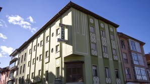 A multi-story building with a green facade, a sign for a hotel, and a sign for a cafeteria. - Pension Monteverde (Cangas de Onis)