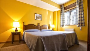 A hotel room with two beds, a bedside table with a lamp, a window with curtains, and a wall-mounted air conditioner. - Pension Monteverde (Cangas de Onis)