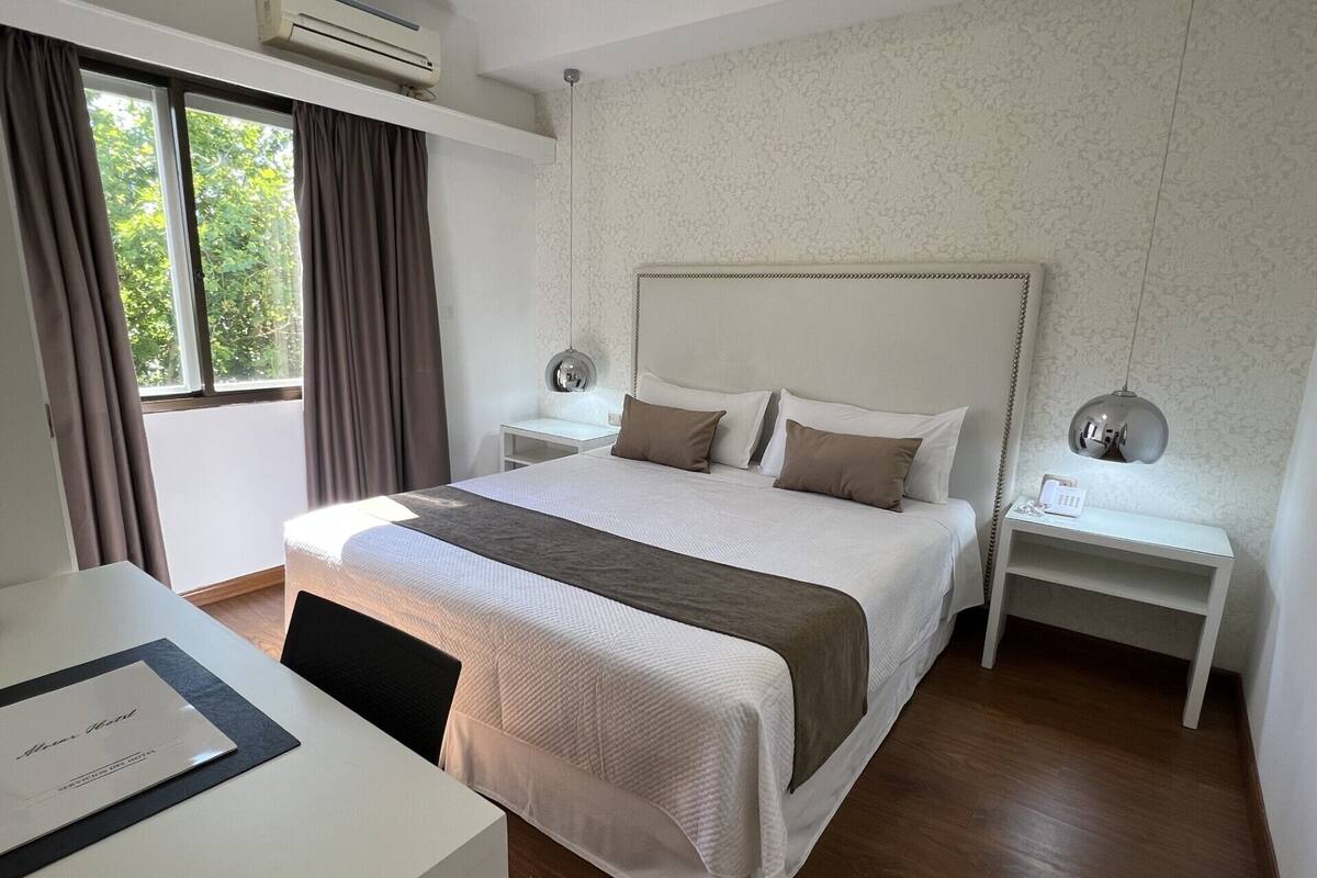 A hotel room with a large bed, two bedside tables, a desk, and a window with curtains.