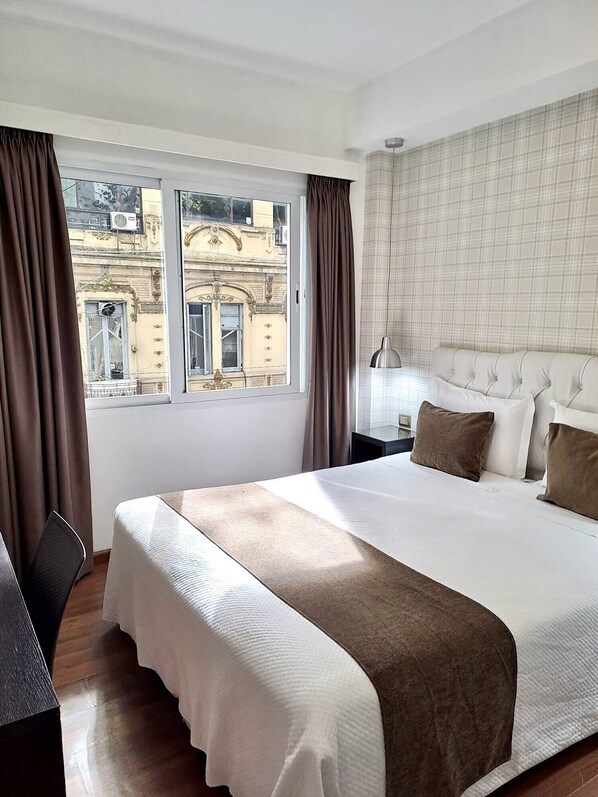 A hotel room with a large bed, a desk, and a view of a building through the window.