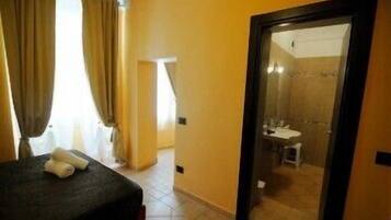 A hotel room with a bed, a bathroom visible through an open door, and a window with curtains.