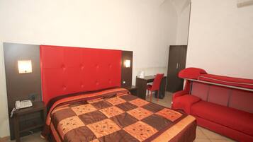 Quarto de hotel com uma cama grande, cabeceira vermelha, escrivaninha com cadeira e sofá vermelho.