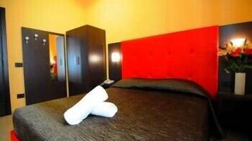 A modern bedroom with a bed, a wardrobe, and a red accent wall.