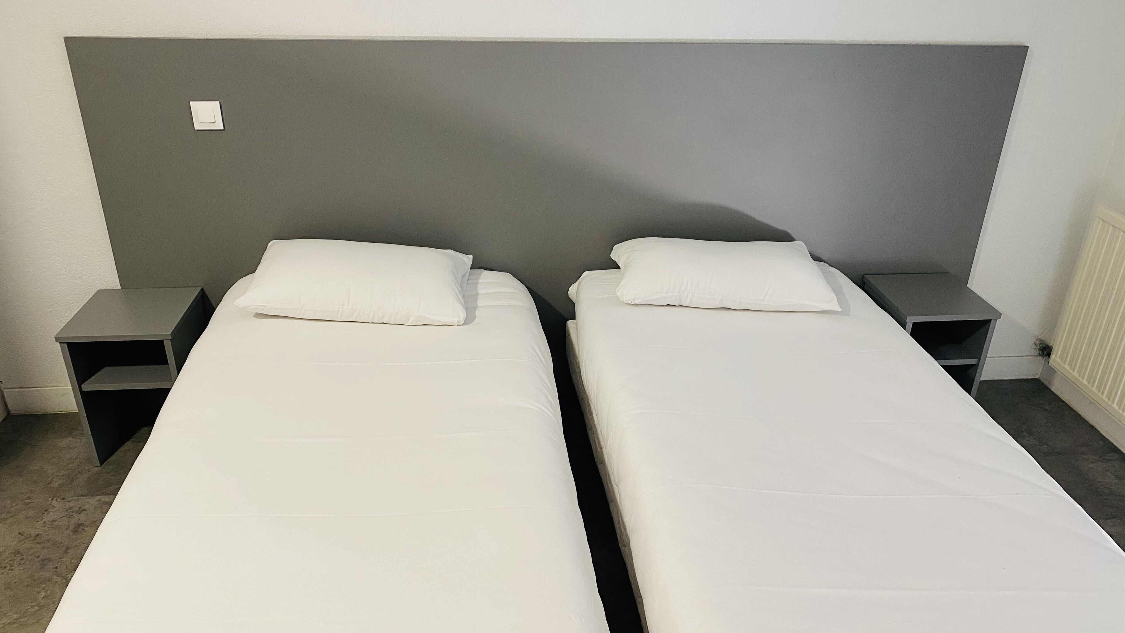 Habitación doble con dos camas individuales, cada una con una mesita de noche y almohada.
