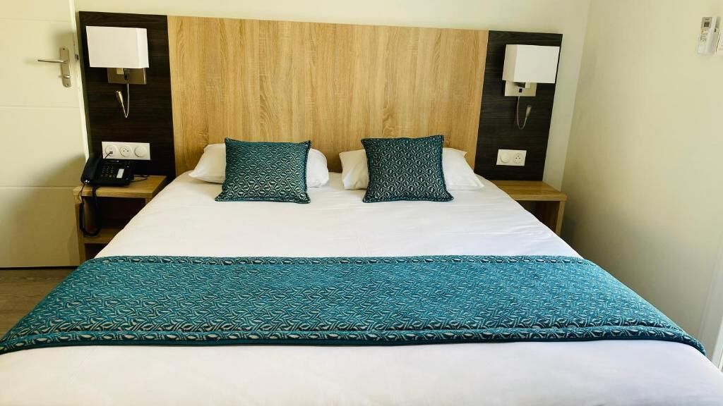 Habitación de hotel con una cama grande, dos mesitas de noche con lámparas, un teléfono y un cabecero de madera.