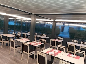 Enjoy a comfortable dining experience in this stylish space with tables, chairs, and large windows offering a view of the outdoor area.