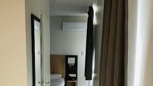 A narrow hallway with a bed at the end, a wooden floor, and a window with curtains. - Hôtel Martinez Grenay (Grenay)