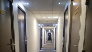 A long, narrow hotel corridor with doors on both sides, a carpeted floor, and recessed lighting on the ceiling. - Hôtel Martinez Grenay (Grenay)