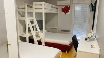 A bunk bed room with a ladder, a small desk, and a window with blinds.