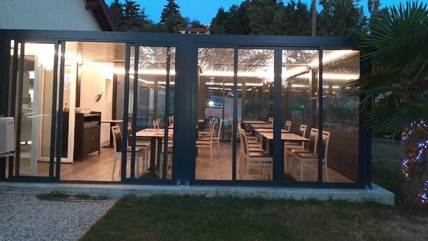A modern building with a glass facade, interior dining area with tables and chairs, and a visible kitchen area. - Hôtel Martinez Grenay (Grenay)