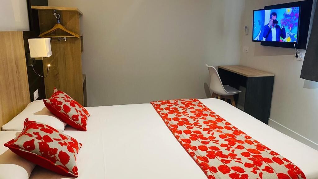 A hotel room with a bed, a desk, a chair, a TV, and a wardrobe.