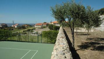 Ein Tennisplatz mit Steinmauer, Olivenbäumen und Häusern im Hintergrund.
