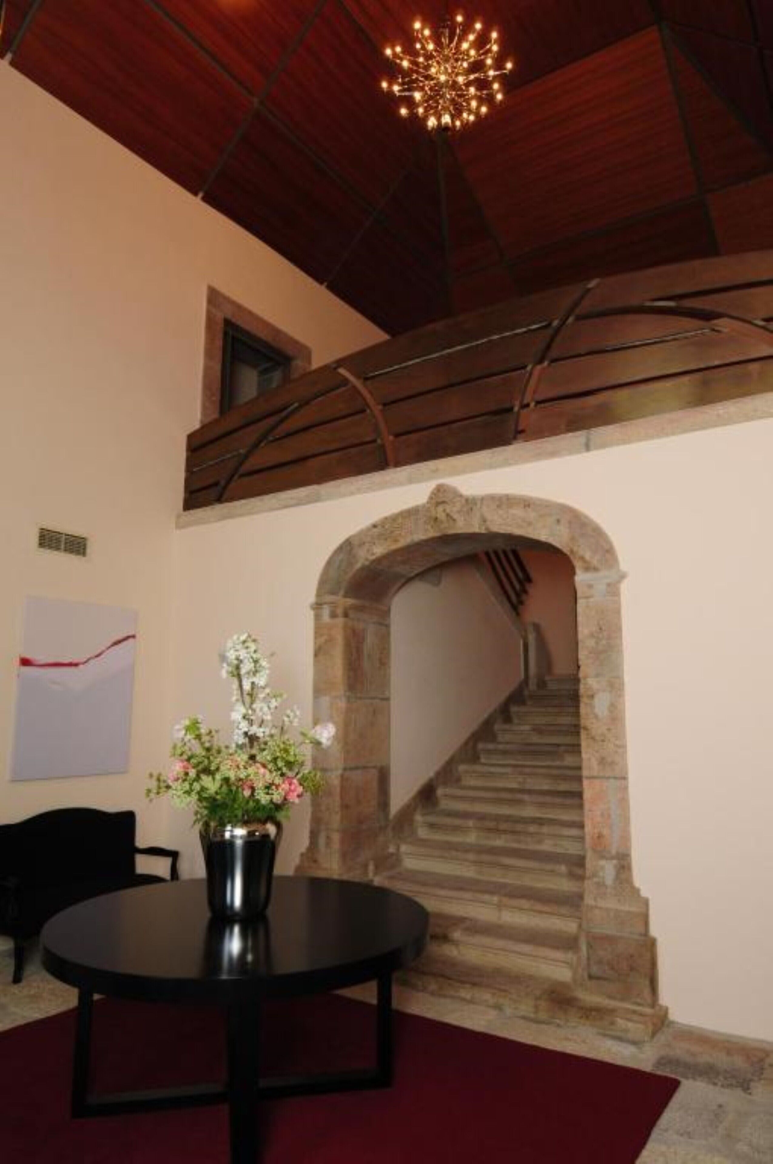 Una habitación con una escalera de piedra, una mesa redonda con un jarrón de flores y una araña.