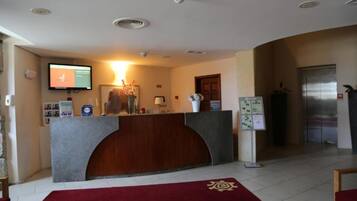 Zona de recepción con mostrador de madera, televisor de pantalla plana, refrigerador y alfombra roja.