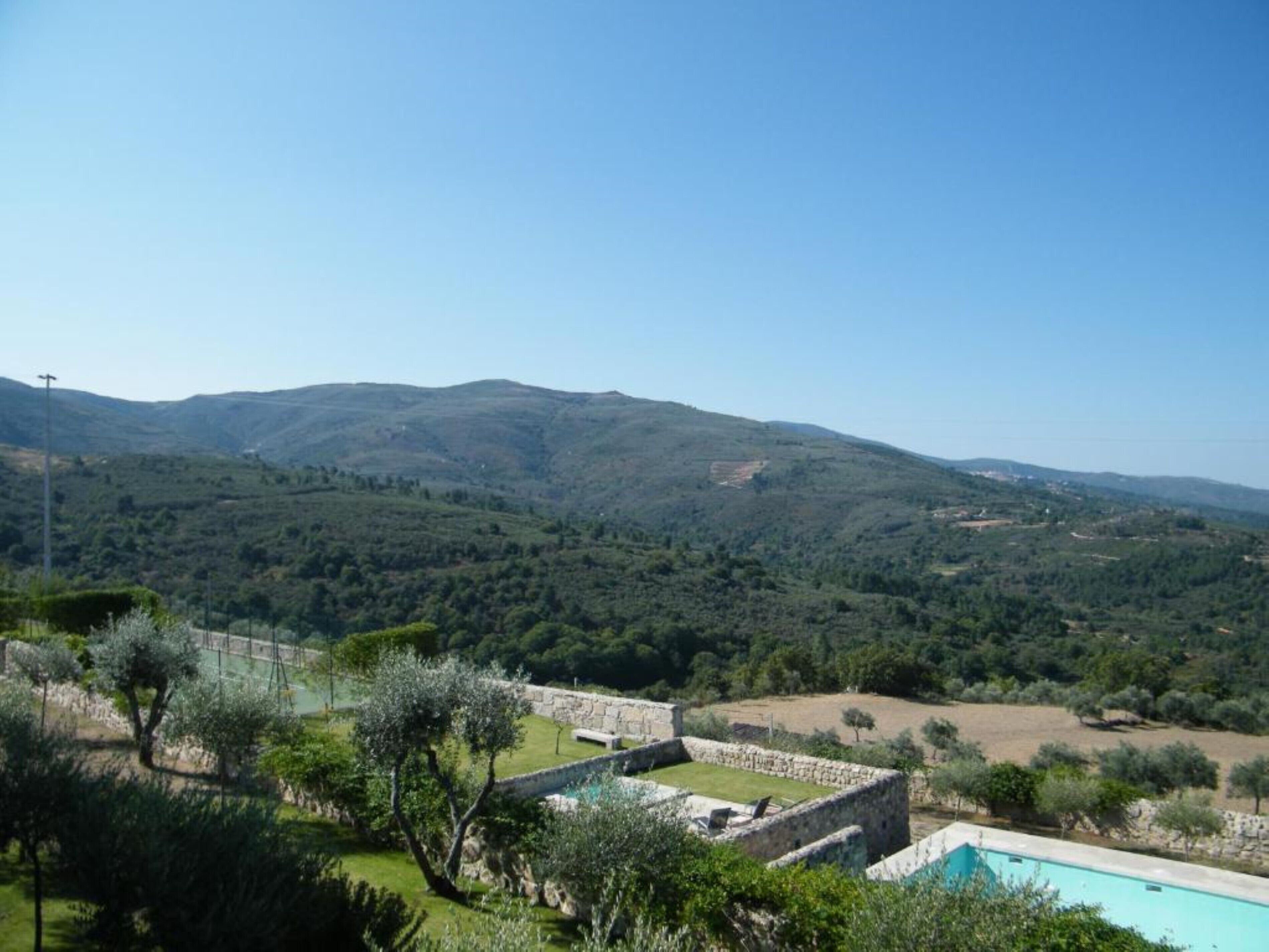 A pool surrounded by stone walls, with a view of rolling hills and a clear sky.