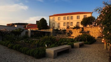 A courtyard with a stone wall, a bench, and a building with a red roof.