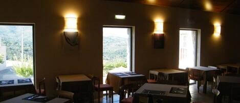 A restaurant with tables and chairs, warm lighting, and large windows offering a view of the outdoors.