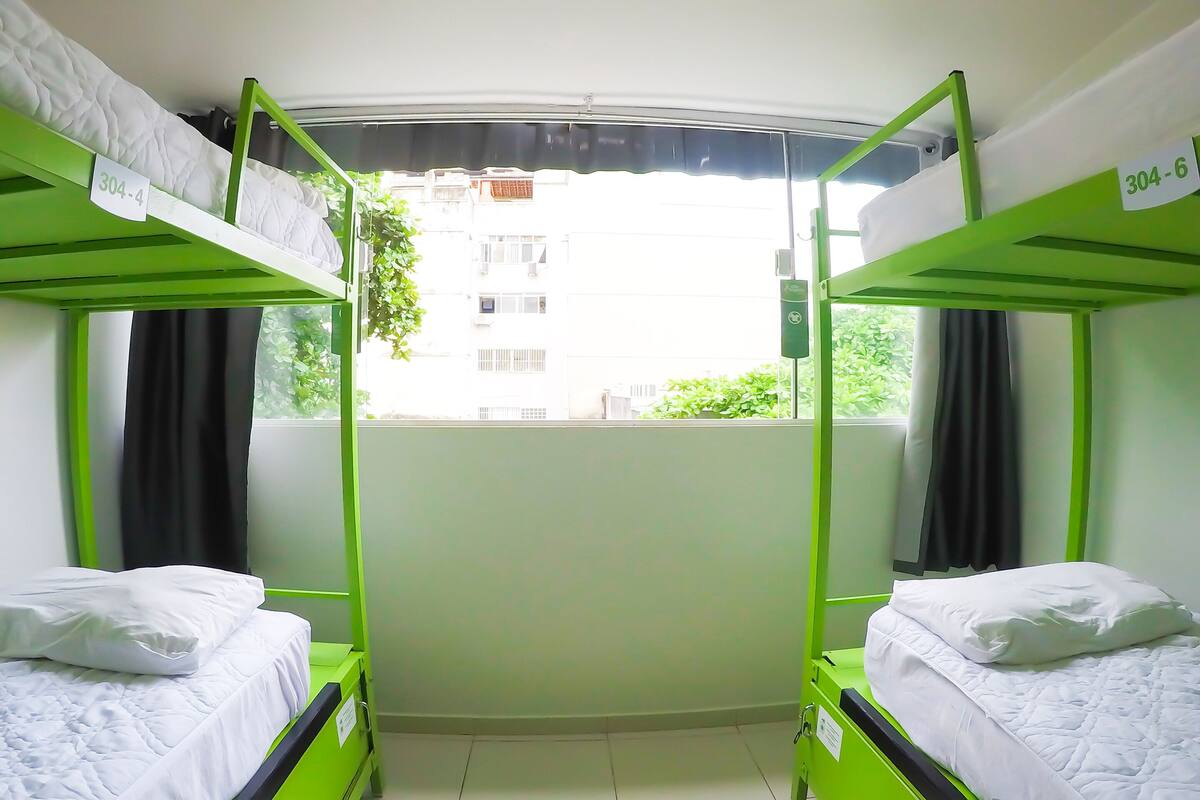 Une chambre de dortoir avec des lits superposés, une fenêtre avec des rideaux et une vue sur les bâtiments environnants.