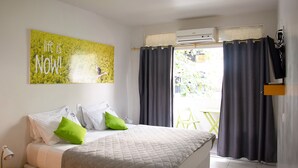 Une chambre à coucher avec un lit, un oreiller vert, un oreiller blanc, une couvre-lit matelassée grise, un climatiseur fixé au mur et une fenêtre avec des rideaux foncés.