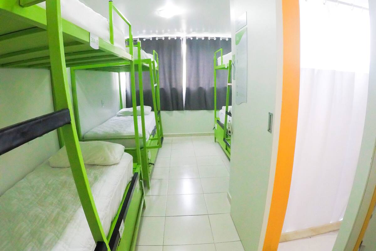 Une chambre de dortoir avec des lits superposés, un sol carrelé et une fenêtre recouverte d’un rideau.