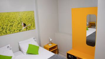 A hotel room with a bed, a nightstand, a mirror, and a wall-mounted picture of a person in a field.