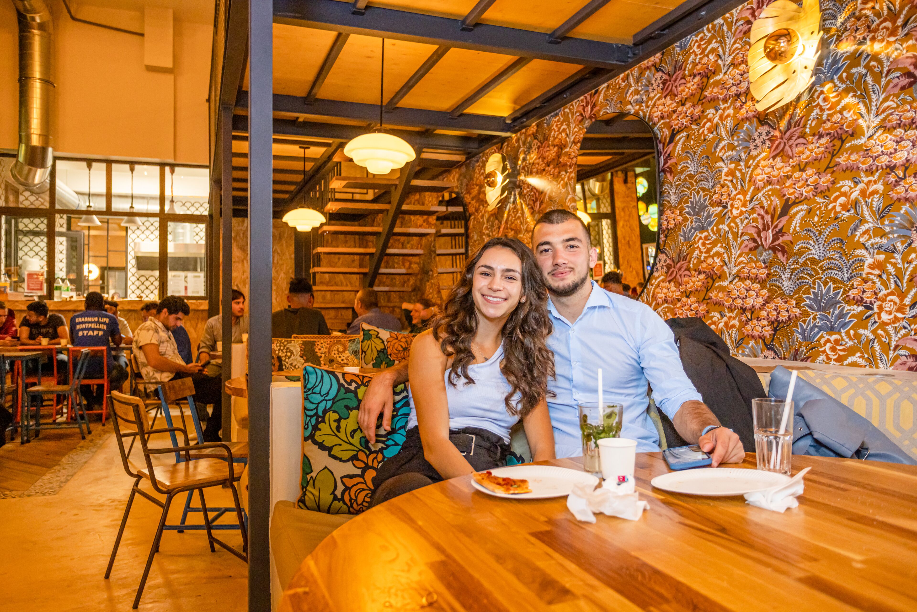 Interior de restaurante con mesas y sillas de madera, y una pared con diseño.