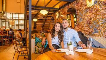 Interior de restaurante con mesas y sillas de madera, y una pared con diseño.